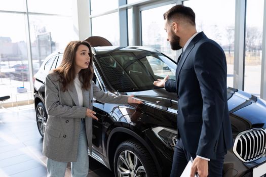 young woman buyer arguing in car dealership with consultant.