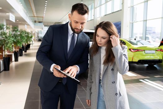an employee of a car dealership helps to sort out a car insurance buyer woman.