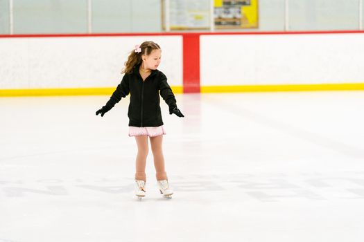 Little girl practicing figure skating on an indoor ice skating rink.