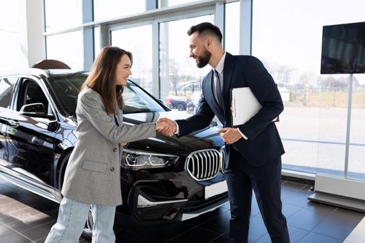 manager and buyer in a car dealership sign documents on the purchase of a new car.