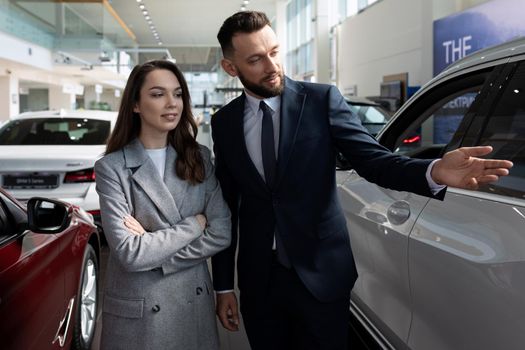 car dealership representative presenting a new car to a young woman buyer.