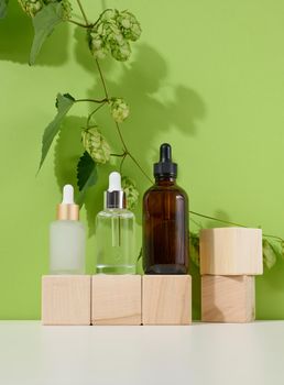 Three glass bottles with pipettes for cosmetics, acids, oils on a green background. Empty containers, product advertising