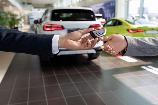 car dealership consultant handing over the keys to the buyer close-up on the background of new cars.