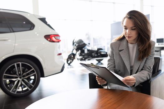 a young woman reads a contract for the purchase of a new car in a car dealership on credit.