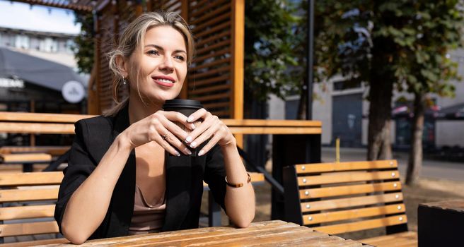 confident business woman drinking coffee in a street cafe with a smile on her face.