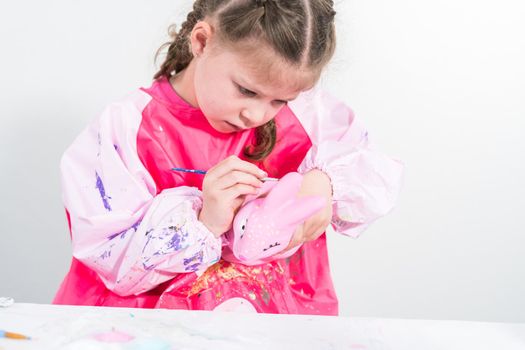 Homeschooling during COVID-19 lockdown. Little girl painting paper mache Easter bunny figurine with acrylic paint.