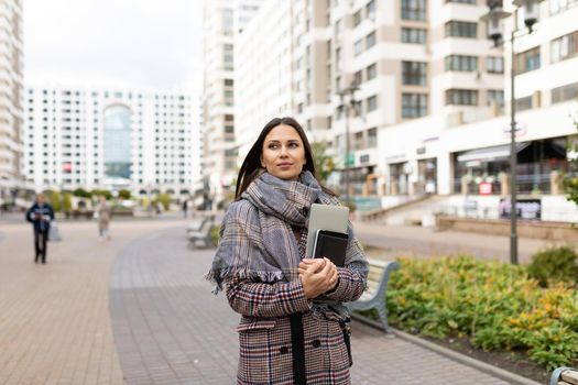 young female student with a laptop and a notebook on the background of the city panorama.