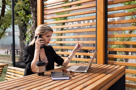 portrait of a young businesswoman talking on the phone behind a laptop outdoors.
