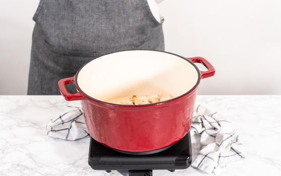 Mixing ingredients in an enameled dutch oven to prepare chicken alfredo pasta.
