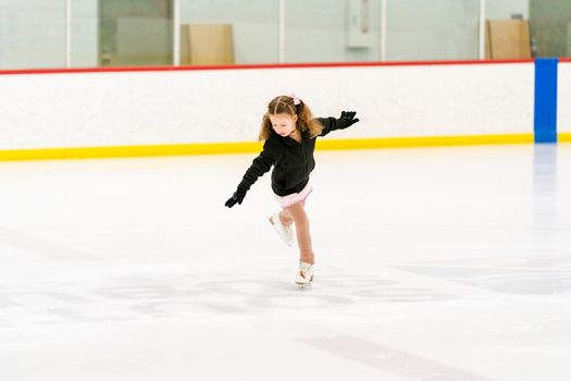 Little girl practicing figure skating on an indoor ice skating rink.