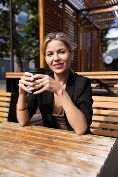 young middle-aged woman with a smile looking at the camera in a street cafe with a cup of coffee.