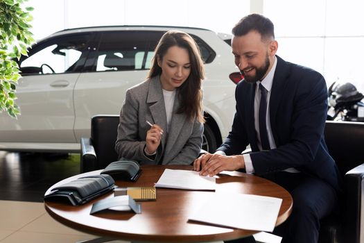 a young woman buys her first car in a car dealership and signs a contract to buy insurance.