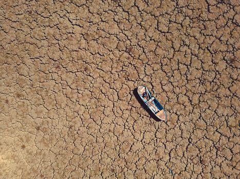Abandoned row boat on cracked soil on lake bed dried up due to global warming and drought.