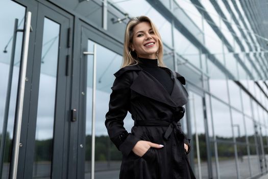 charming businesswoman in a black business coat at the door to the office building looking at the camera with a smile.
