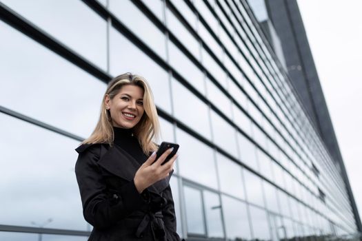 young woman Businessman with a phone next to the glass facade of an office building.