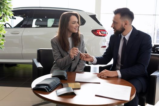 male manager selling a new car to a young woman in a car dealership.