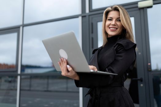 successfully confident businesswoman works online on a laptop against the backdrop of an office building.