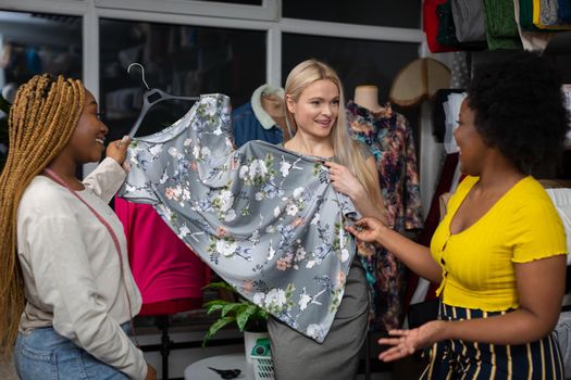 A European woman is thinking about buying a dress with a floral pattern. Two African women offer a dress from the new summer stylish collection.