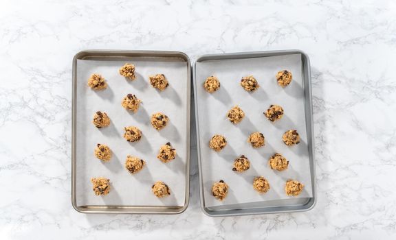 Flat lay. Scooping cookie dough with dough scoop into a baking sheet lined with parchment paper to bake soft oatmeal raisin walnut cookies.