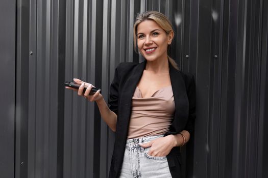 charming middle-aged business woman with a charming smile against a gray wall in her hands holds a mobile phone.