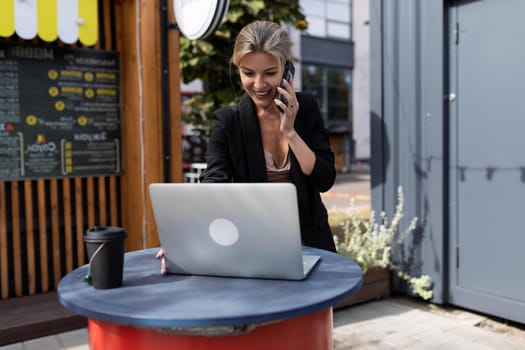 young successful woman working at a laptop at a table in a street cafe.