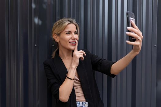 middle-aged woman in the office making secrets by video call on the background of a gray wall.