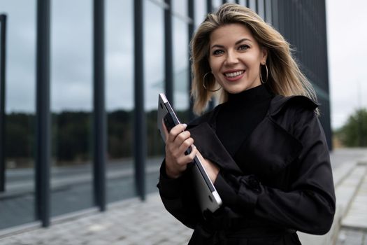 office employee woman with a tablet in her hands hurries to work with a smile on her face against the backdrop of the city.