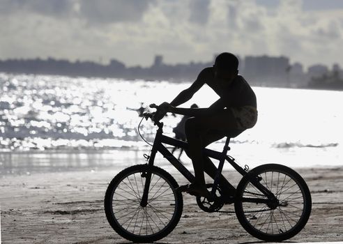 salvador, bahia, brazil - december 22, 2015: young man is seen riding a bicycle on the sand of Placafor beach in Salvador city.