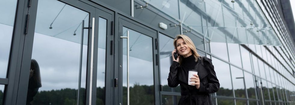 young woman businessman talking on the phone with a glass of coffee on the background of an office building.