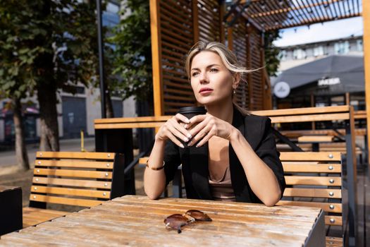 stylish pensive middle-aged woman drinking coffee in a cafe on the street.