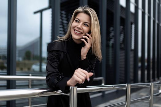 a woman manager speaks on a mobile phone against the backdrop of an office modern building made of glass.