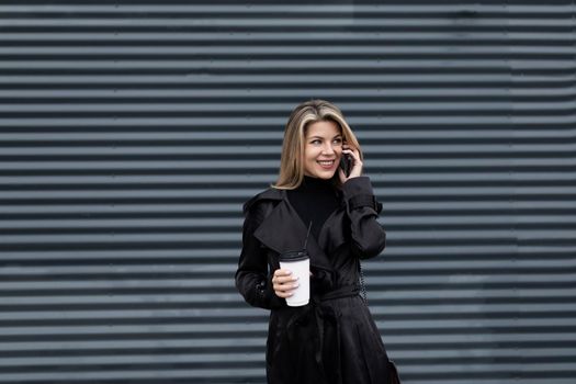 portrait of a female executive in black business clothes with a glass of coffee talking on the phone against a dark wall.