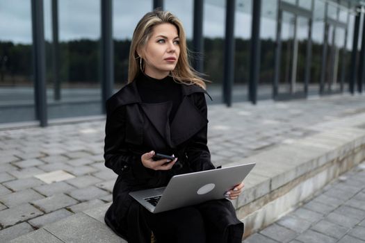 modern successful woman businessman working online on laptop next to office glass building.