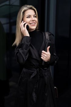 portrait of a business woman on the background of a black glass building with a smile looking into the distance.