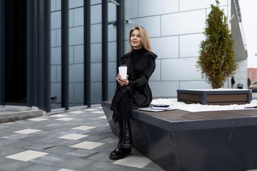 business woman pause coffee next to office building.