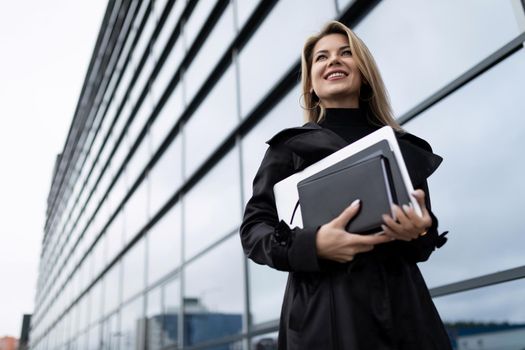 A business woman goes to work with a laptop under her arm and a smile on her face.