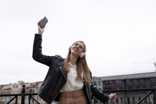 happy young woman with a mobile phone in her hands and headphones dances against the backdrop of the city panorama.