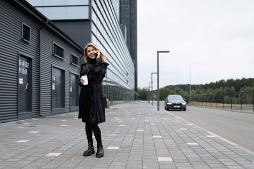 successful business woman talking on a mobile phone with a cup of coffee in her hands on the background of the office.