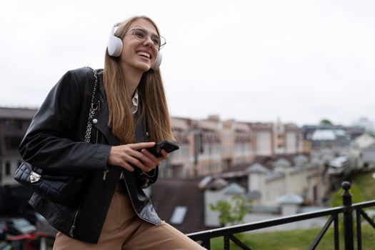 a young student listens to pleasant music against the backdrop of the urban landscape in headphones with a phone in her hands.