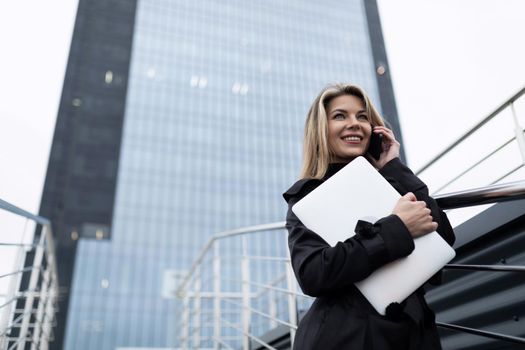 portrait of a businesswoman against the background of a non-glass facade of an office building with a laptop in her hands.