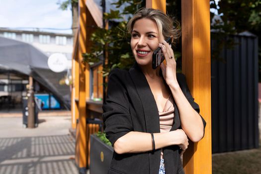 middle-aged woman talking on the phone on the background of the city looks away with a smile on her face.