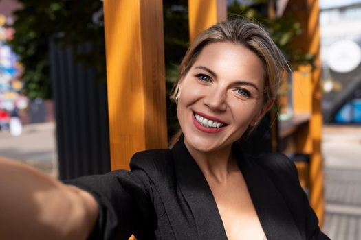 young middle-aged businesswoman taking a selfie in the sun during the day in the city.