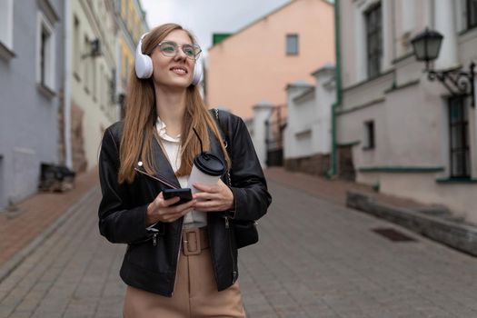 young woman Tourist in headphones with a mobile phone walks through the old city.