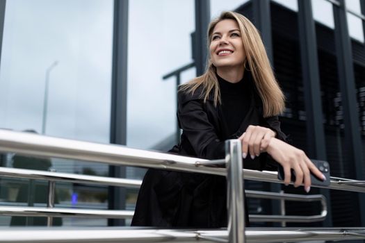 Business successful middle-aged blonde woman with a smile looks into the distance against the backdrop of an office building.