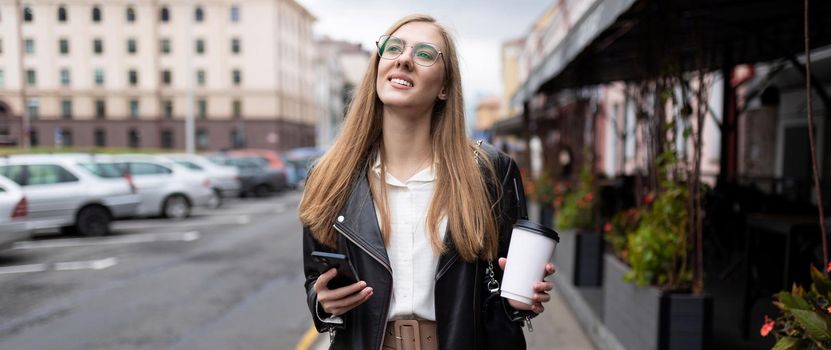 young strong woman walking around the city with a cup of coffee in her hands dreamily looks into the distance.