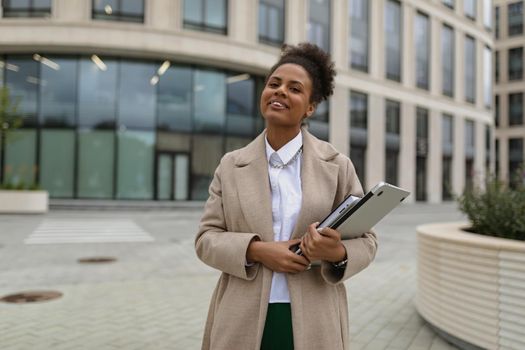 young woman Businessman with a laptop in a gray coat on the background of a city building.