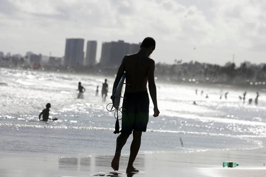salvador, bahia, brazil - december 22, 2015: young man is seen walking with surfboard on the sand of Placafor beach in Salvador city.
