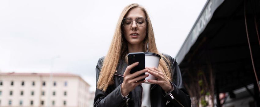 portrait of a serious young woman with a cup of coffee looking at a mobile phone.