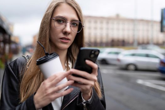 portrait of a serious young woman with a cup of coffee looking at a mobile phone.