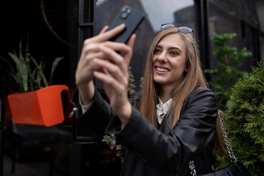young woman blogger takes a selfie next to a popular cafe in the city.
